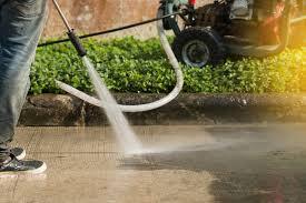 Worker pressure washing sidewalk with compresser in background