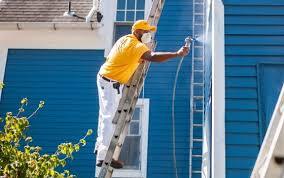 Painter on ladder spraying house with blue paint