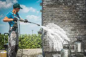 Worker using pressure washer to clean brick wall