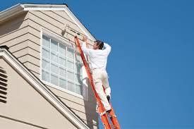 Painter on high ladder using roller to paint house