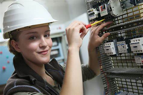 Female electrician smiling in front of electrical panel